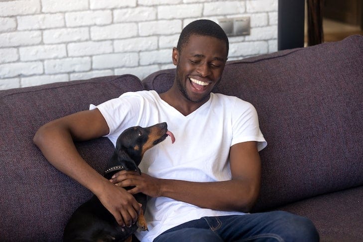 A black man plays with a Daschund dog